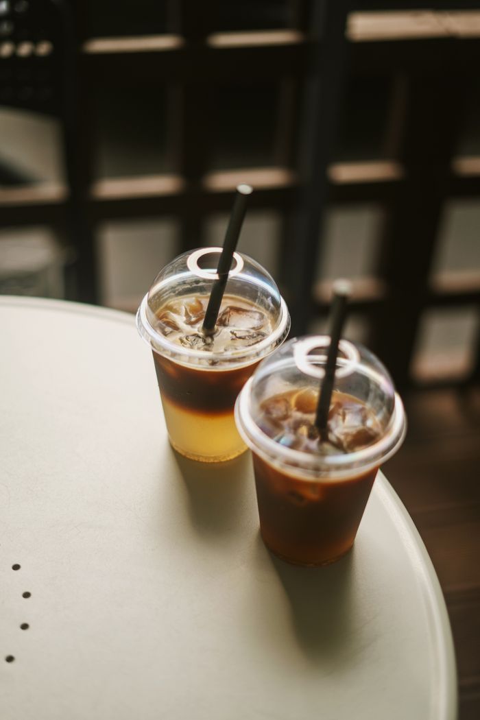 Two iced beverages in plastic cups with straws on a sunny day outdoor table.