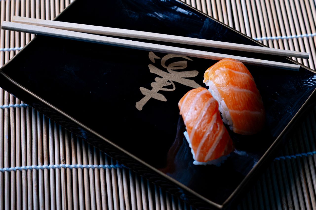 Two salmon nigiri sushi pieces on a black plate with chopsticks, Belo Horizonte.