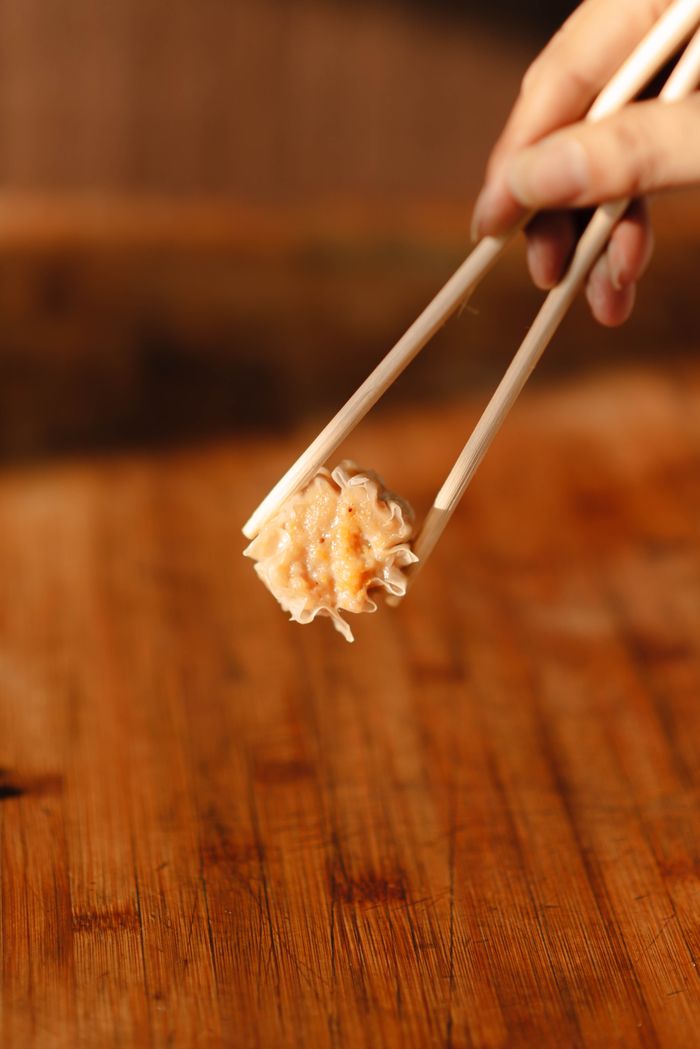 A delicious dumpling held by chopsticks on a wooden background, showcasing Asian cuisine.