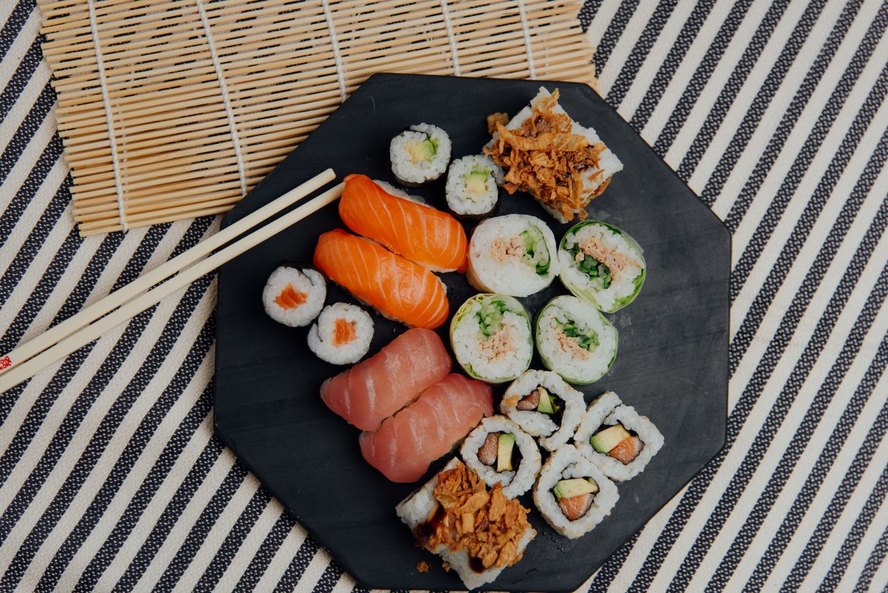 Top view of assorted tasty sushi and rolls served on table with chopsticks and rolling bamboo mat in light room